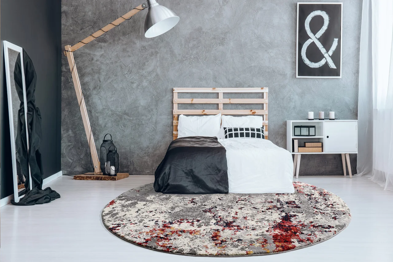 Illustration - Ihr Experte für schönes Wohnen - Ein runder rot gemusterter Teppich liegt im Schlafzimmer halb unter dem Bett.