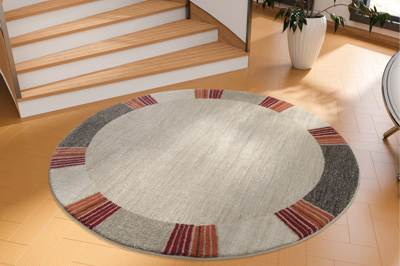 Illustration - Ihr Experte für schönes Wohnen - Ein runder Teppich mit einer bunten Borte liegt im Flur vor einer Treppe.